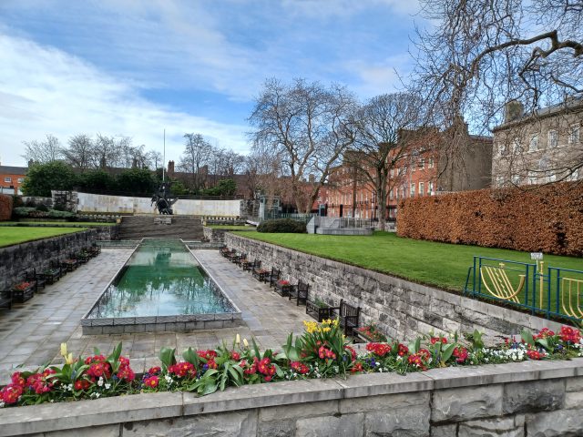 view of a long shallow pool, and steps leading up to a statue of the Children of Lir