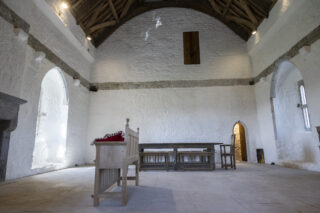 wide view of the high-ceilinged room with white walls, wooden flooring, and a dining table in the centre