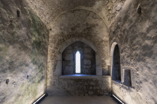 view of the interior walls of the chapel, with a narrow window in the centre letting in natural light.