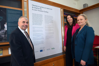 3 people stand around an information panel smiling at the camera