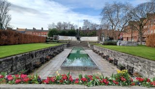 wide shot of the Garden of Remembrance with the pool of water in the centre, flowers in the foreground, and the lir statue and sky in the background