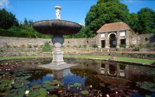 Close up of fountain and pond at Heywood Gardens with loggia in background with red tiled roof.