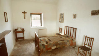 Bedroom in Pearse’s cottage with frames on wall and crucifix
