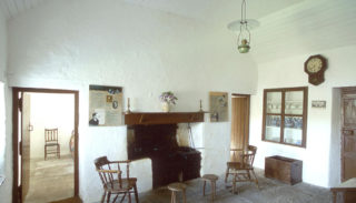 Kitchen inside Pearse’s cottage with stove and cabinet with china