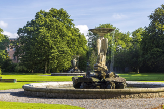 Two female statues in their respective fountains stand facing each other, across the grass
