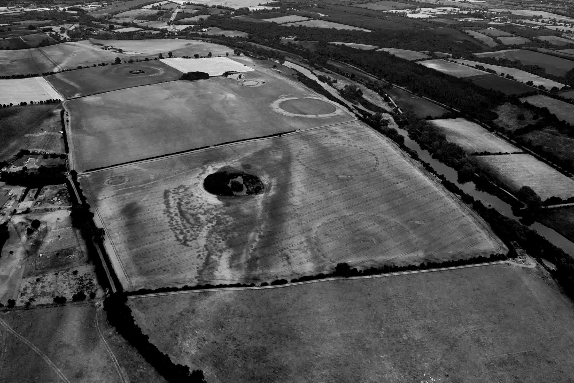 View across the Newgrange floodplain from the west, showing the alignment of the henges (right). The dark linear band indicates differential crop growth over a major palaeochannel, within which there is an extant pond likely to have been of ritual significance in the Neolithic.