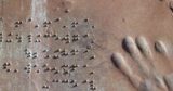 A bronze relief sculpture of braille text and hand print