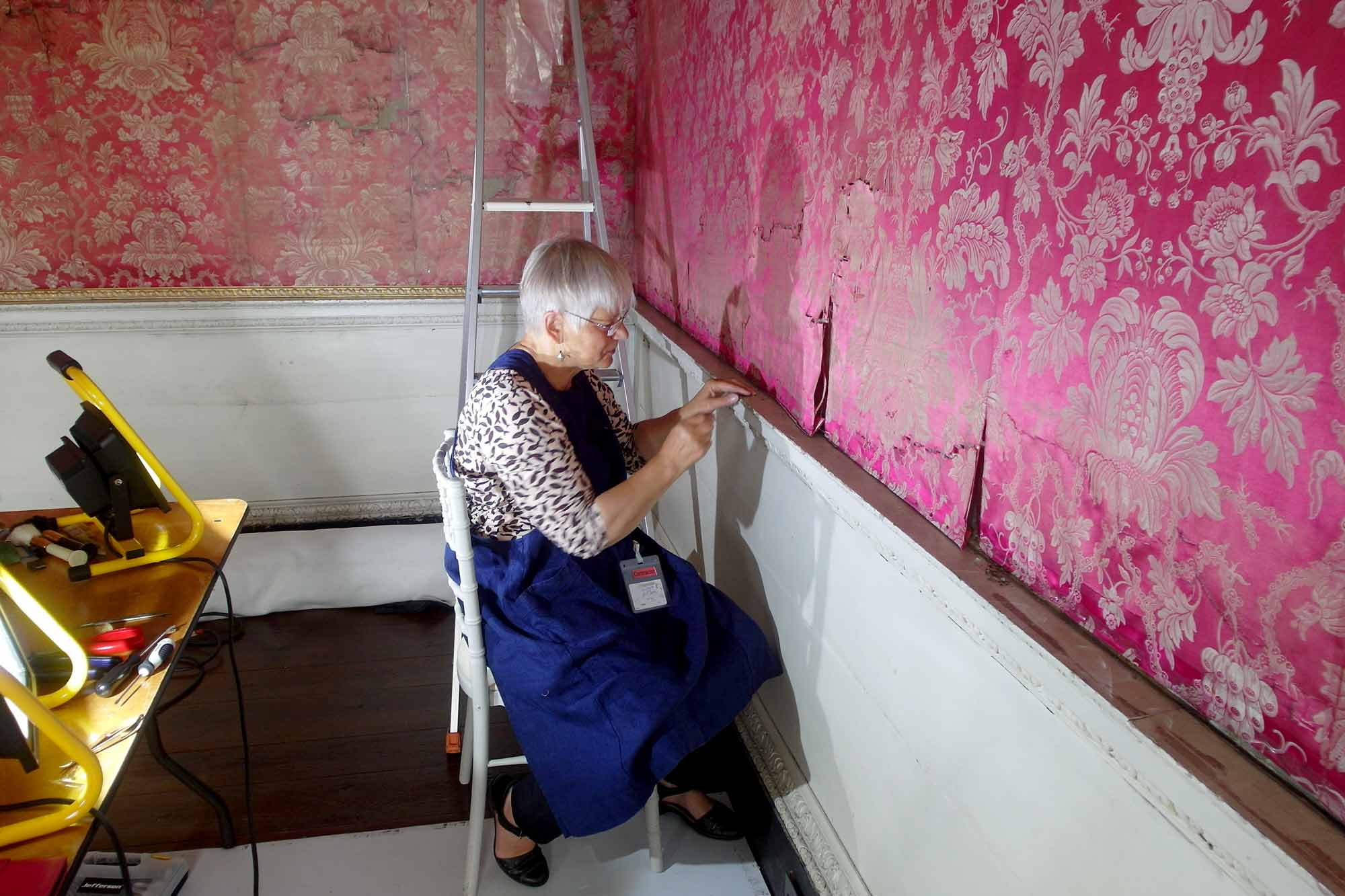 Ksynia Marko is removing tacks at the bottom of a panel on the West Wall in order to release fabric folded back on itself and in this way to close up a horizontal tear running across the silk higher up