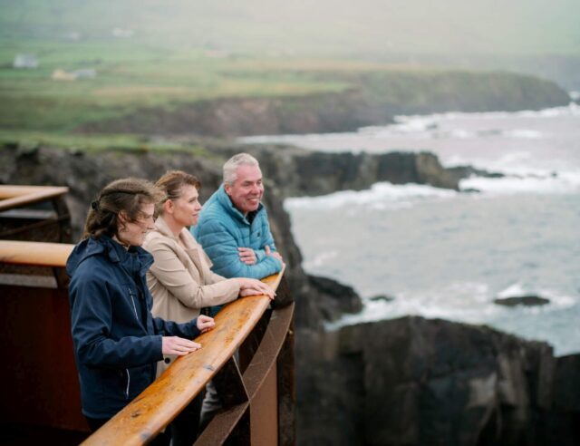 3 people stand on a viewing platform overlooking the Atlantic Ocean