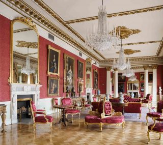 A large room with extravagant furniture and chandeliers. There are large paintings adorning the wall on one side