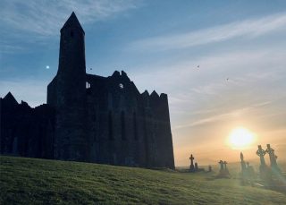 A watery sunset over the graveyard beside the Rock of Cashel castle. The gravestones and the castle are backlit and appear ominous.