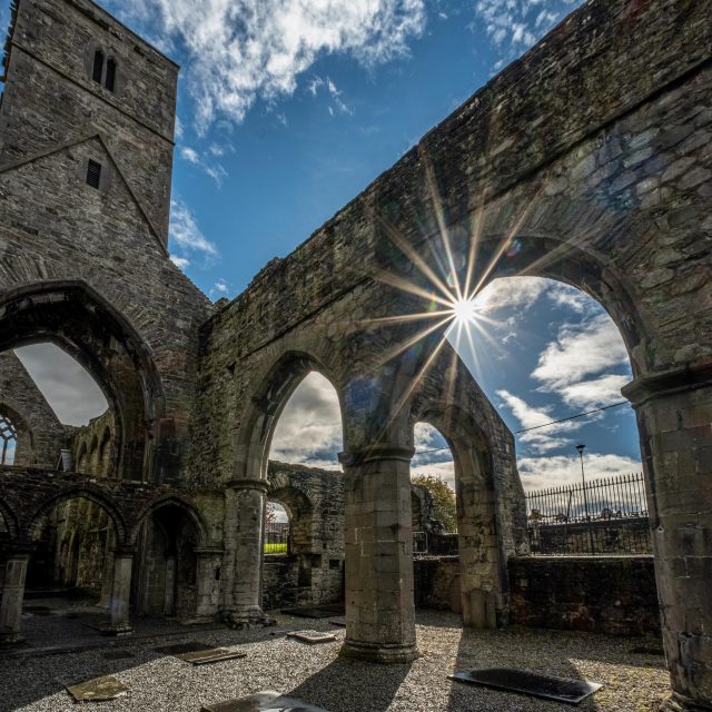 the roofless abbey and its arches are backdropped by the glinting sun