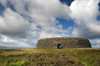 Two people are exiting the stone fort to the lavender fields surrounding it. The clouds are large and fluffy, overtaking the image
