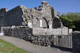 A close-up of some of the ruins of Murrisk Abbey. There appears to be a shrine on one side of the ruin, with closed gates leading into it.