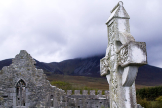 A celtic style cross stands prominently in the foreground of the image with the ruins of an augustinian friary surrounding it. The backdrop to this is Croagh Patrick, the mountains shrouded in mist, giving the image a mystical feel.