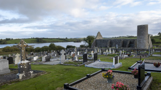 A graveyard sits in the foreground of the image, with the abbey and tower in the background, and the lake off to the left side