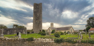Wide shot of the round tower and church behind it, backdropped by thick blue/grey clouds