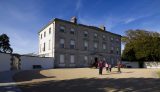 a group of 4 people walk up to the entrance of the house that is now the Battle of the Boyne museum. Two canons frame the outside of the door.