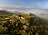 aerial view of fort ruins, perched high on a hill, the surrounding landscape shrouded in mist