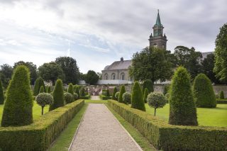 An exterior image of the Royal Hospital Kilmainham. The photo is taken from the gardens, the steeple of the hospital is visible in the background. Hedges lines the path through the gardens.