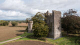 a square shaped castle stands across from a smaller round turret, with a tree growing between the two