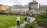 An image of the Dubh Linn Gardens. The Record Tower of Dublin Castle and the State Apartments are visible in the background. Three people walk in the gardens.