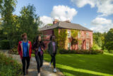 An exterior image of Glebe House. Three teenagers walk towards the camera in the foreground of the image.