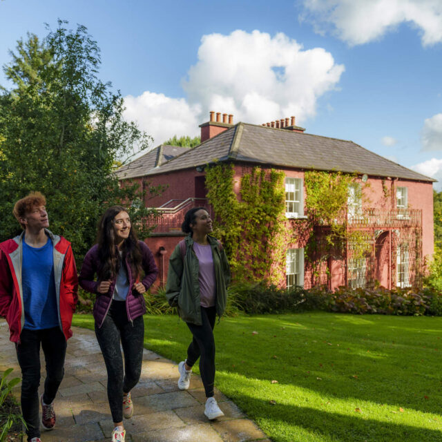 An exterior image of Glebe House. Three teenagers walk towards the camera in the foreground of the image.