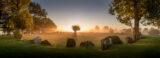 a wide circle of standing stones with the sun setting in front.