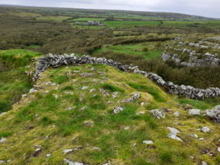 A stone fort situated among the rugged terrain of the Burren, with a house in the far distance