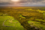 the stone fort perched on the edge. The surrounding field landscape lit by the sun peeking through the darkened sky.