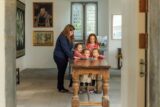 A female guide and four young girls explore a historic room at Ormond Castle during Heritage Week. The group is gathered around a wooden table, examining a book. Historical portraits and artifacts adorn the walls in the background.