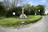 A designed stone cross sitting within a patch of grass beside the road