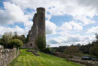 Side view of Dunmoe Castle ruins, with a cross in the centre of the green