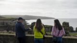 A man is talking to two women as they overlook the harbour view