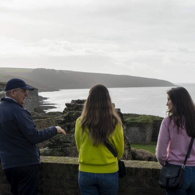 A man is talking to two women as they overlook the harbour view