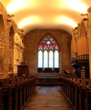 interior image of St. Audoen's church looking at the stained glass window, and the pews on either side