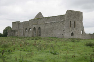 the ruins of the abbey within a wild field, the arches of the cloister visible, and the open sections of where the windows used to be still held within the stone