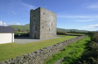 A rectangle stone castle standing among the short grass, backdropped by a blue sky with wispy clouds