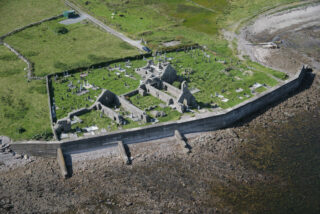 an aerial view of the abbey by the bay, with graves surrounding the remaining ruins