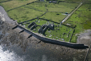 an aerial view of the abbey by the bay, with graves surrounding the remaining ruins