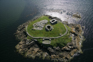 aerial view of Church island in the middle of the sea, the monuments sitting on the grassy mound of this small island