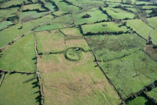 A ringfort almost hidden within the vast green landscape. It is an aerial view of the ringfort situated within fields.