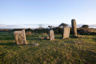 Four standing stones in the middle of a field, with a view of the surrounding landscape