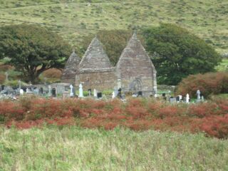 The roofless church set within the mountainous backdrop, with grave crosses surrounding it.