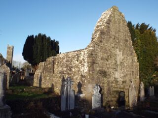 a small roofless church, with a few tombstones beside it. The church has a pointed triangular shape at the front.