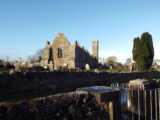 a church with a tower protruding from the back, the ruins are now roofless, and are standing among a graveyard