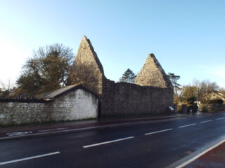 a long rectangular shaped church, now roofless, stands near the side of the road.