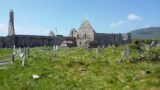 side profile of the abbey, with some graves to its right side, and the mountains as the backdrop