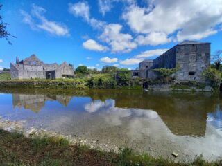 a wide shot of the friary from across the river, with an industrial-like building just opposite the friary